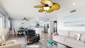 A modern living room with a glass coffee table, a sofa, a leather chair, and a ceiling fan. - Seventh floor condo with pool access, washer&dryer, ocean view, & central AC (Fort Walton Beach)