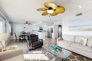 A modern living room with a glass coffee table, a sofa, a leather chair, and a ceiling fan. - Seventh floor condo with pool access, washer&dryer, ocean view, & central AC (Fort Walton Beach)