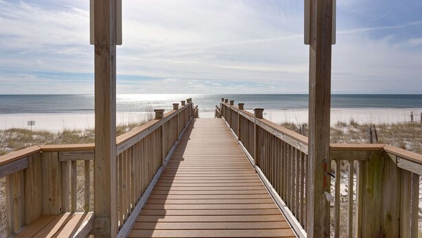 Een houten looppad dat naar een strand leidt, onder een heldere lucht.