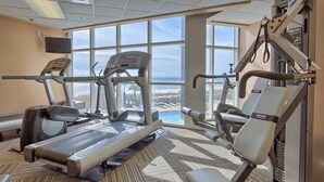 Een sportschool met cardio-apparatuur, krachttoestellen en een groot raam met uitzicht op de oceaan.