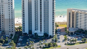 Een hoog hotel met meerdere verdiepingen, een parkeerplaats en uitzicht op het strand.