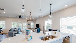 Une cuisine moderne dotée d’un grand îlot central, d’appareils électroménagers en acier inoxydable et de luminaires suspendus.