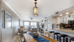 A spacious dining area with a long wooden table, blue table runner, and white chairs. - Gulf-front condo with heated pool, fitness room & beach chairs - close to dining (Fort Walton Beach)