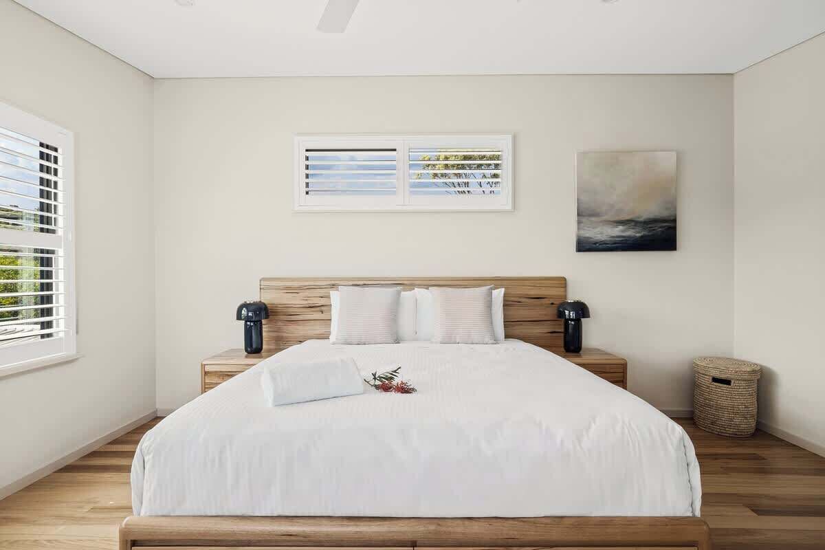 Une chambre à coucher avec un lit en bois, une literie blanche, deux lampes fixées au mur et une œuvre d’art encadrée au-dessus du lit.