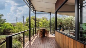 Une terrasse en bois avec une table et des chaises, de grandes fenêtres et une vue sur la verdure et les collines.
