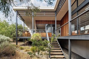 Een modern gebouw met een overdekt buitengebied, een trap en een tuin met diverse planten.