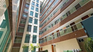 A multi-story building with a central atrium, glass railings, and a mix of brick and glass facades. - Mar Bello Plaza #207 por Carpediem (Cabedelo)