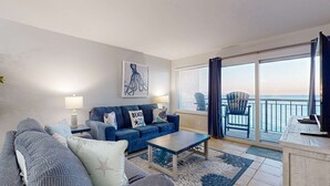 Ein Wohnzimmer mit einem blauen Sofa, einem grauen Sofa, einem Couchtisch und einem großen Fenster mit Meerblick.