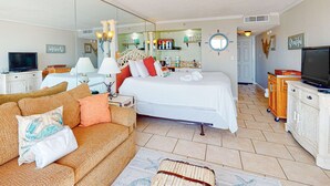 Una camera d'albergo con un letto, un divano, una televisione, uno specchio e un angolo cottura sullo sfondo.