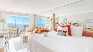 Una camera d'albergo con un letto grande, un balcone vista mare, una zona pranzo e un salotto con vista.