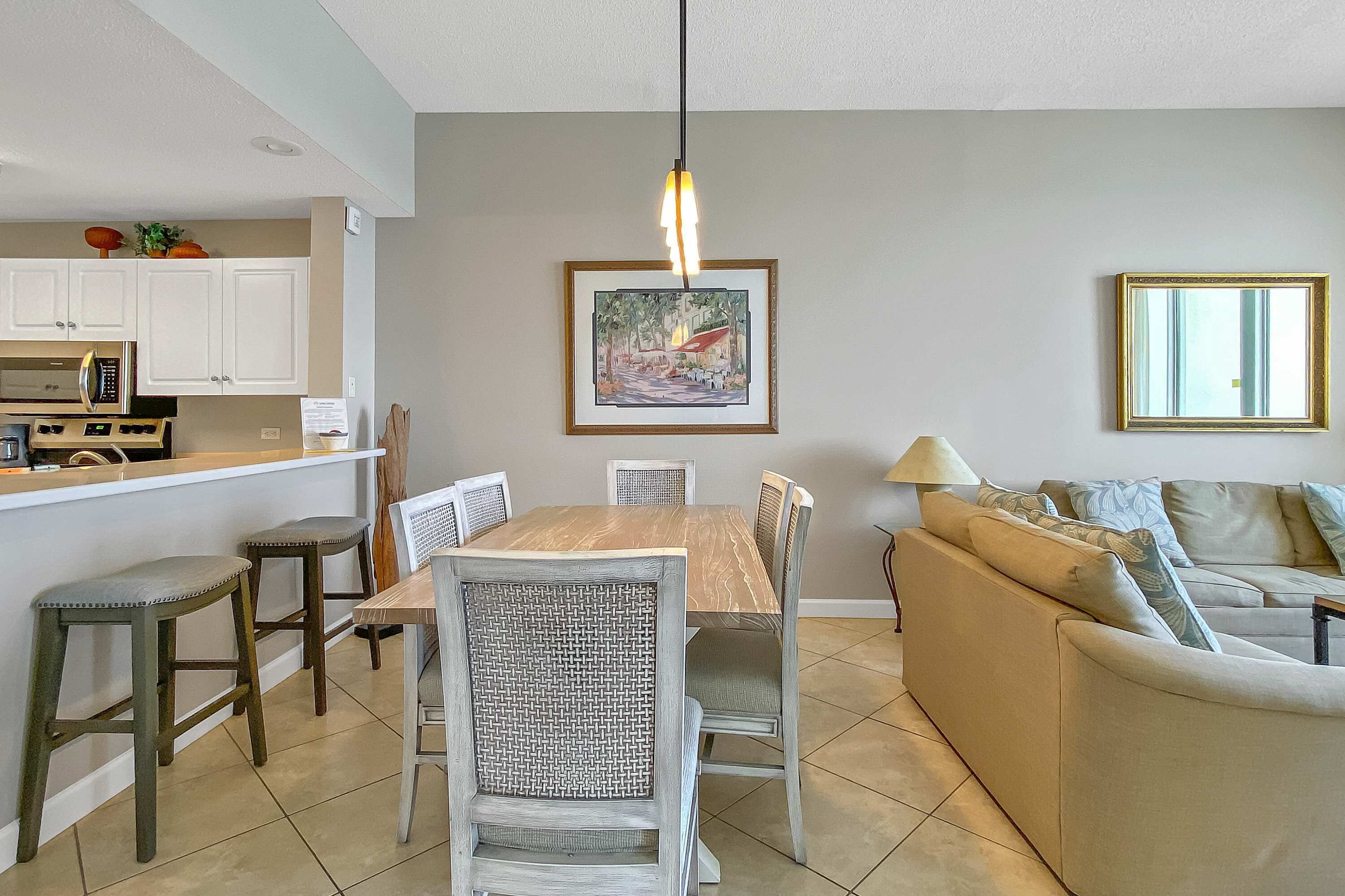 A dining area with a wooden table and chairs, a kitchen with white cabinets, and a living room with a beige sofa.