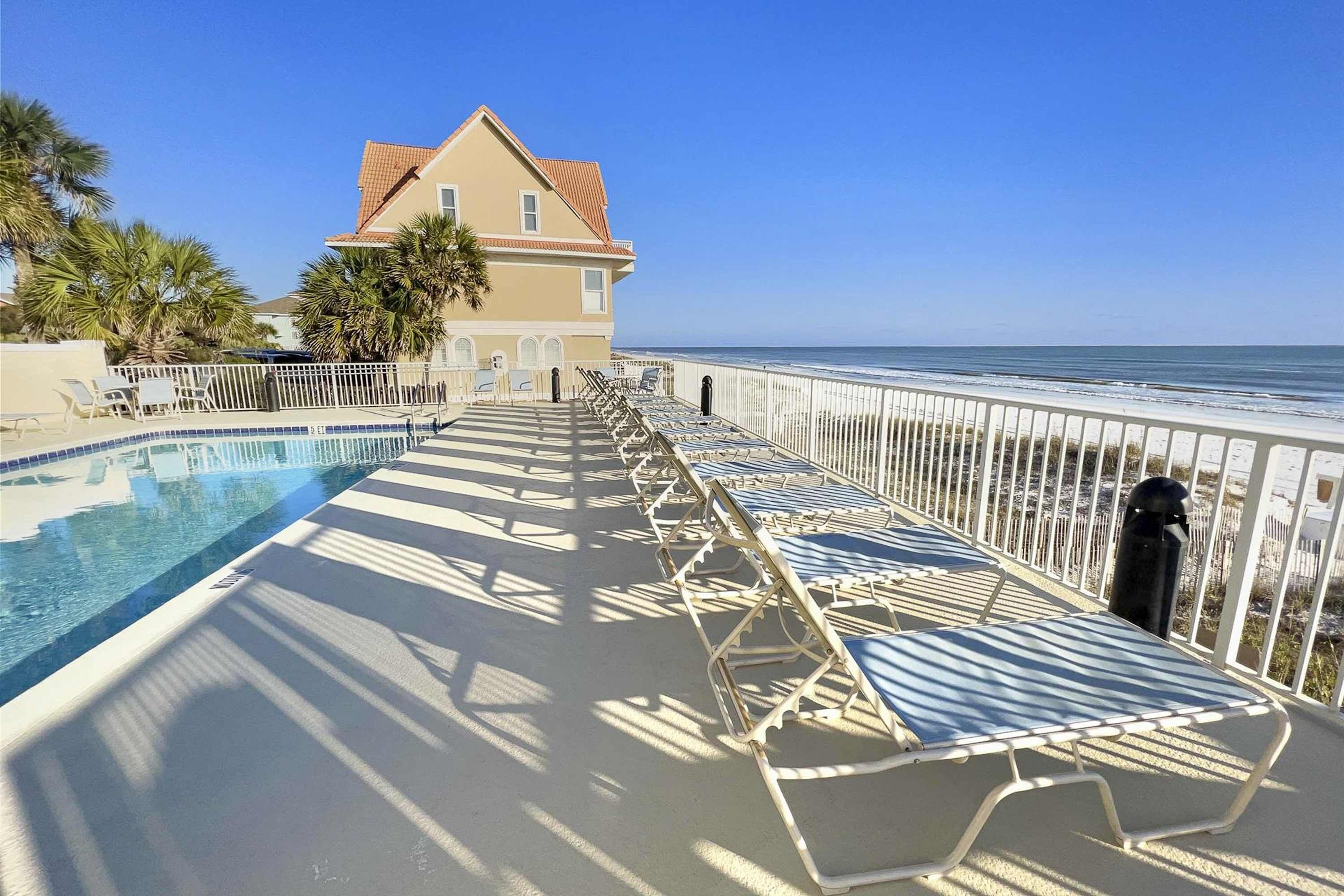 A poolside area with lounge chairs, a swimming pool, and a view of the ocean.