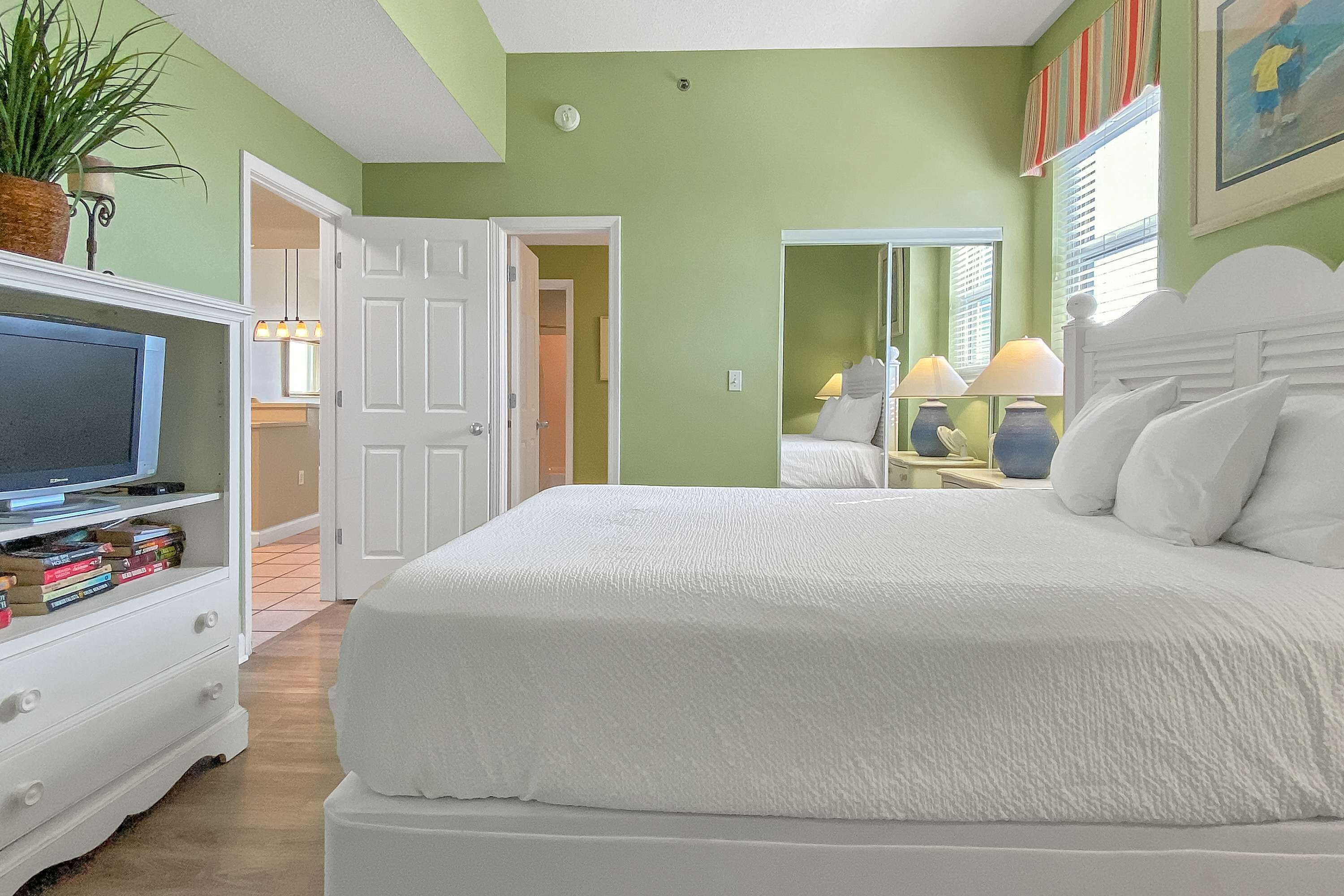 Un dormitorio con una cama grande, un televisor sobre un aparador y una puerta que da a otra habitación.