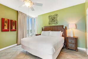 A bedroom with a large bed, a nightstand with a lamp, and a decorative wall piece. - Stylish oceanfront West Tower corner condo - 3 balconies, WiFi, & pool/hot tub (Panama City Beach)