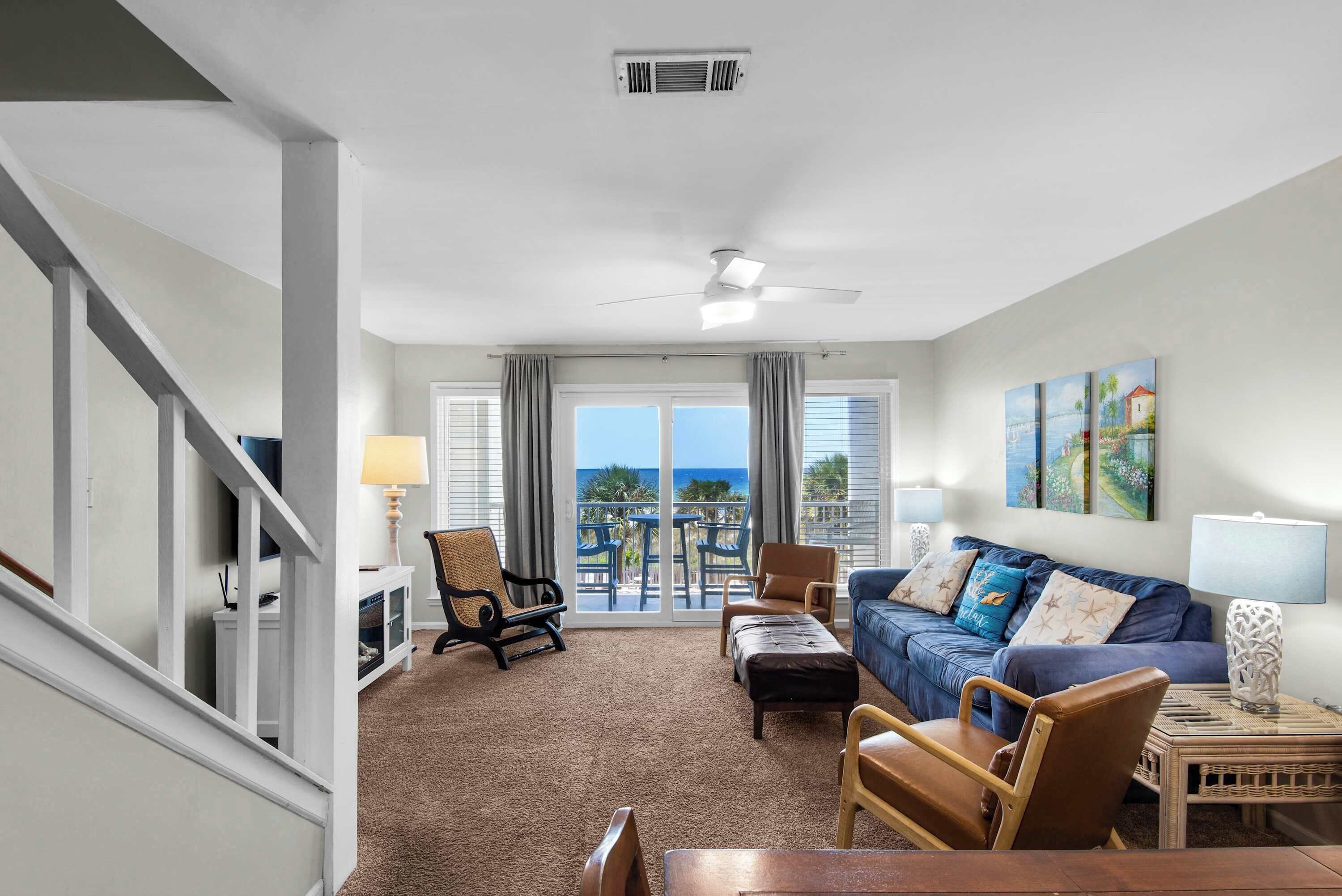 A living room with a sofa, chairs, a coffee table, a lamp, and a view of the ocean through large windows.