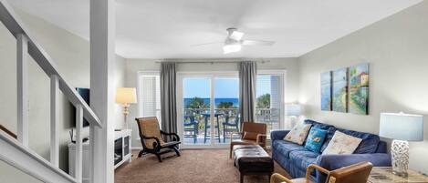 A living room with a sofa, chairs, a coffee table, a lamp, and a view of the ocean through large windows.