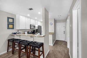 A modern kitchen with white cabinets, a microwave, and a refrigerator. There are three bar stools and a clock on the wall. - 2-story condo with Gulf views, on-site pool, balconies, & easy beach access (Panama City Beach)