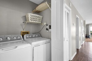 A laundry area with two front-loading washers and dryers, a drying rack, and a wall-mounted laundry basket. - 2-story condo with Gulf views, on-site pool, balconies, & easy beach access (Panama City Beach)