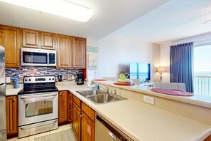 A modern kitchen with wooden cabinets, stainless steel appliances, and a large window with a view. - Cozy & colorful beachfront condo with balcony, pools, & fitness center (Panama City Beach)