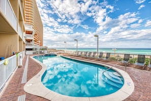A pool area with a clear view of the ocean, a brick pathway, and a building with balconies. - Cozy & colorful beachfront condo with balcony, pools, & fitness center (Panama City Beach)