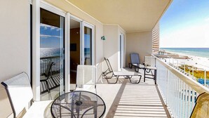 Un balcón con mesa y sillas, vista a la playa y un edificio al fondo.