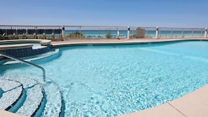 Piscina azul cristalina con diseño moderno, rodeada por una cerca blanca y un cielo despejado.