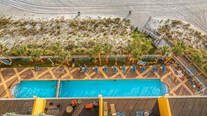 Vue aérienne d’un complexe hôtelier doté d’une grande piscine, de chaises longues et d’une zone de plage.
