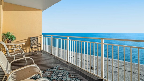 Un balcon avec vue sur la mer, une table, des chaises et un tapis à motifs.