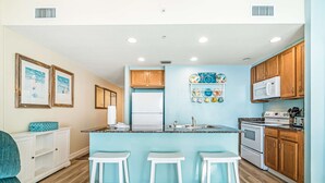 Une cuisine moderne dotée d’un îlot central, de tabourets de bar blancs, de meubles en bois et d’un réfrigérateur blanc.