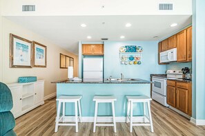 A modern kitchen with a central island, white bar stools, wooden cabinets, and a white refrigerator. - Snow-bird friendly condo with pool & fitness room - walk right out to the sand (Panama City Beach)
