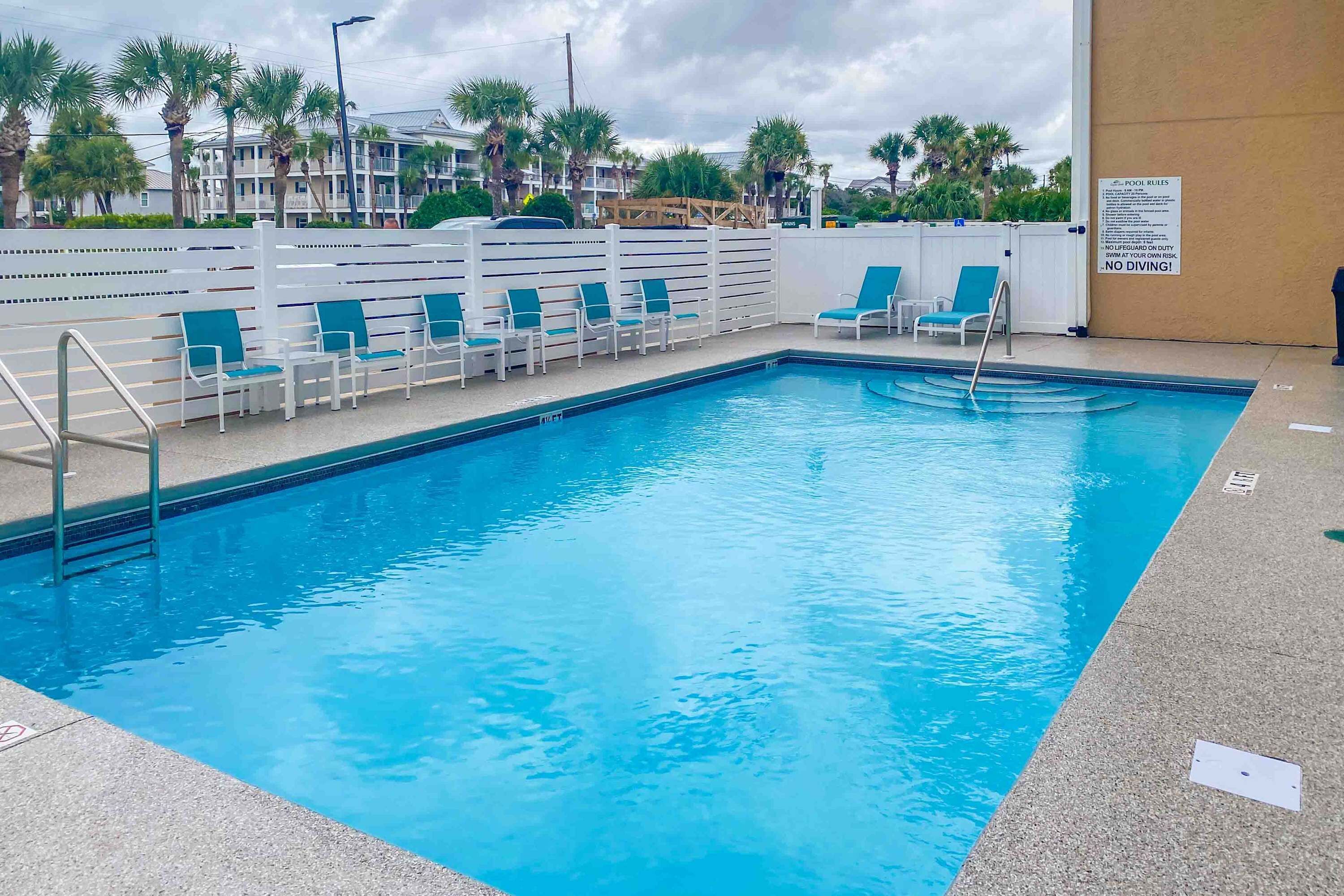 A swimming pool with blue water, surrounded by white lounge chairs and a white fence.