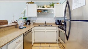 Cocina compacta con armarios blancos, un refrigerador de acero inoxidable, una cafetera y objetos decorativos en los estantes.