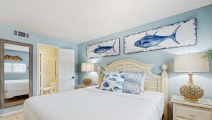 Un dormitorio con una cama grande, dos cuadros de tiburones en la pared, una lámpara de noche y una mesita de noche con cajones.