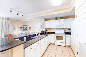 A modern kitchen with white cabinets, a granite countertop, a built-in oven, and a microwave. - Charming, waterfront condo with pools, fitness center & beach access (Panama City Beach)