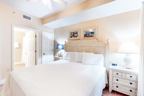 A bedroom with a large bed, a nightstand with a lamp, and two framed pictures on the wall. - Charming, waterfront condo with pools, fitness center & beach access (Panama City Beach)