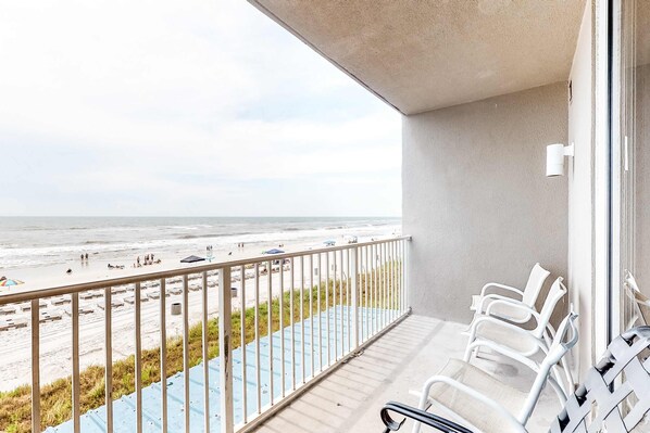 A balcony with a view of the beach, white chairs, and a blue pathway. - Charming, waterfront condo with pools, fitness center & beach access (Panama City Beach)