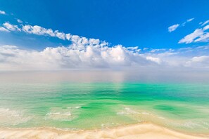 Ein Strand mit klarem türkisblauem Wasser und einem Sandstrand unter blauem Himmel mit vereinzelten Wolken.