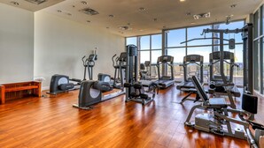 A gym with various exercise machines, a wooden bench, and large windows offering a view. - Updated beachfront retreat with hot tub, outdoor pool & balcony (Panama City Beach)
