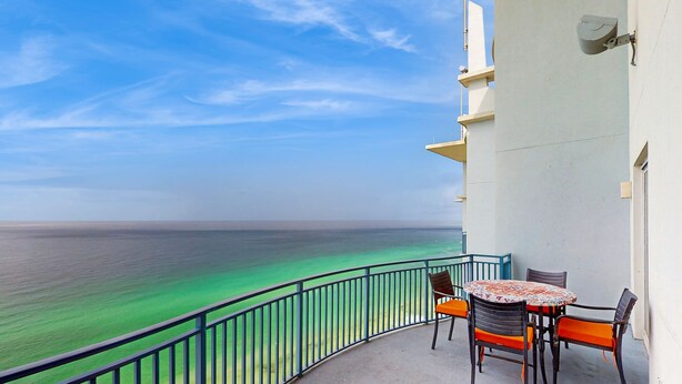 A balcony with a view of the ocean, a round table with chairs, and a small orange bench. - Updated beachfront retreat with hot tub, outdoor pool & balcony (Panama City Beach)