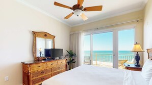 Ein Hotelzimmer mit einem großen Bett, einem Holzschrank, einem Fernseher, einer Pflanze und einem Balkon mit Meerblick.