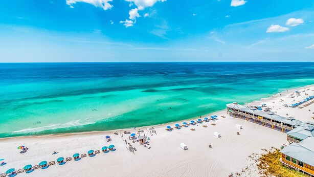 A beach resort with a long row of beach umbrellas and sun loungers, a clear blue sky, and turquoise waters. - Beautiful beachfront getaway with balcony, pools, tennis, and WiFi (Panama City Beach)