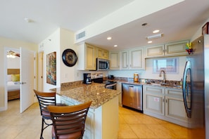 A modern kitchen with granite countertops, stainless steel appliances, and light-colored cabinetry. - Beautiful beachfront getaway with balcony, pools, tennis, and WiFi (Panama City Beach)
