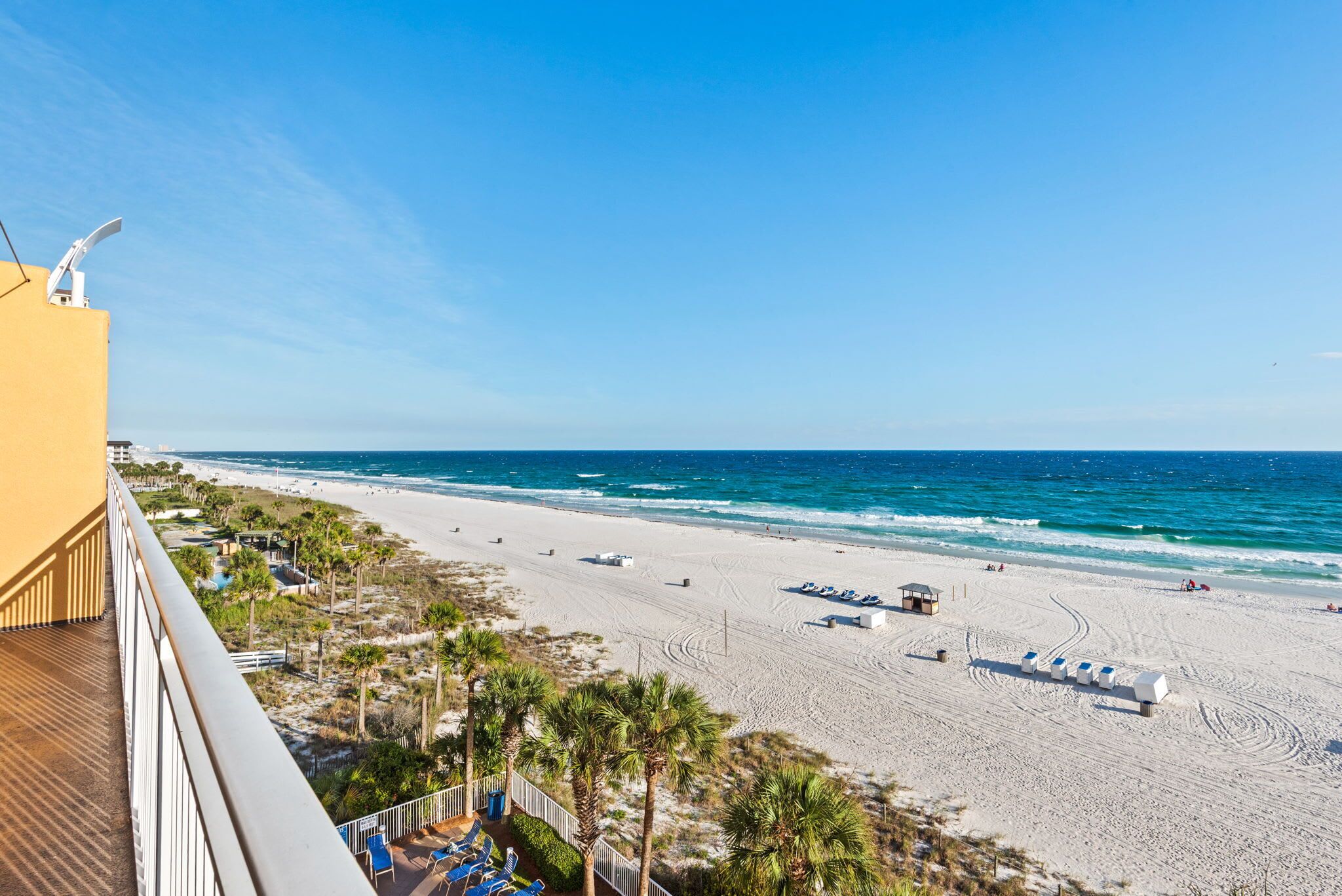 Blick auf einen Strand vom Balkon aus, mit Liegestühlen und Sonnenschirmen, feinem Sand und dem Meer.