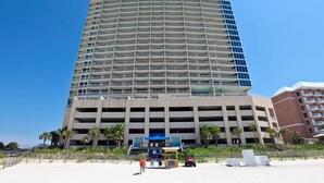 A multi-story hotel with a curved facade, a parking garage below, and a beachside location with palm trees. - Nautical getaway just steps from the beach with pool & hot tub (Panama City Beach)