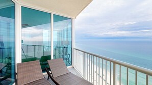 A balcony with two wicker lounge chairs, a glass partition, and a view of the ocean. - Nautical getaway just steps from the beach with pool & hot tub (Panama City Beach)