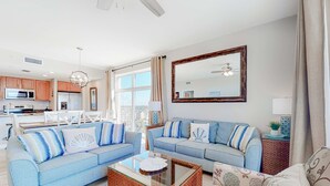 Ein modernes Wohnzimmer mit zwei hellblauen Sofas, einem Couchtisch aus Glas und einer Küche im Hintergrund.