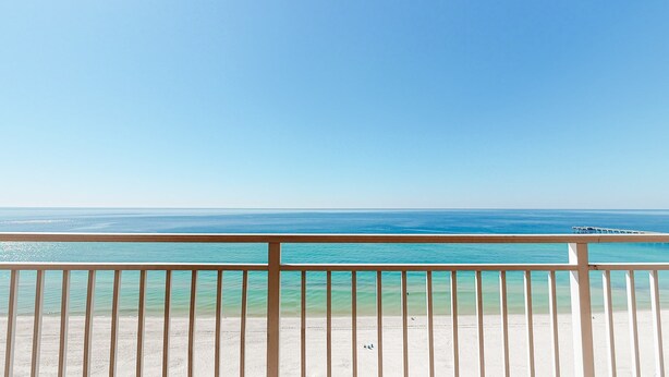 Blick auf einen Strand mit einer Holzbrüstung und klarem türkisblauem Wasser.