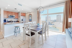 A modern kitchen with wooden cabinets, a stainless steel refrigerator, and a dining area with a large window offering a city view. - Oceanfront, 7th-floor condo with pool, ocean view & high-speed WiFi (Panama City Beach)