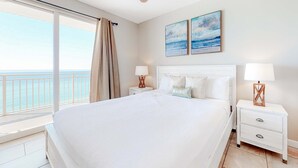 Ein Schlafzimmer mit einem großen Bett, zwei Nachttischen, einem Deckenventilator und Blick auf den Ozean.