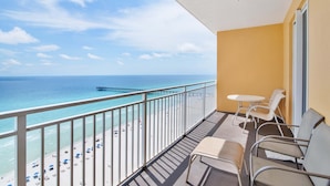 Een balkon met uitzicht op het strand en de oceaan, een tafel met stoelen, en een raam met uitzicht op de pier.